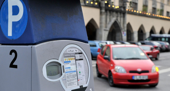 Parkscheinautomat am Straßenautomat. Unscharf im Hinergrund parkt ein rotes Auto ein.