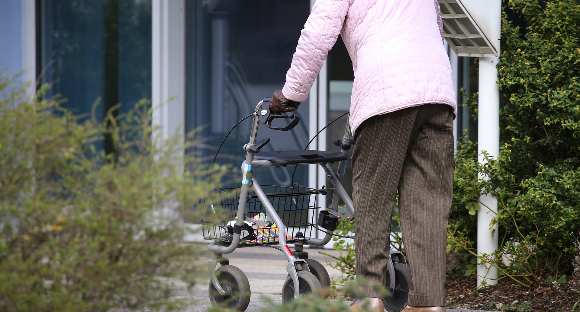 Ältere Frau mit Rollator vor Eingang eines Senioren-Wohnstiftes