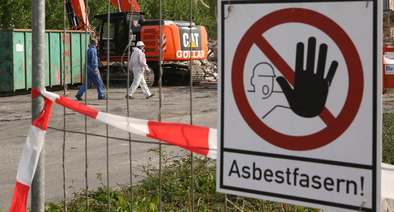 Auf einem Sammelplatz, auf dem asbestbelasteter Schutt lagert, warnt ein Schild: „Asbestfasern!“. (Foto: © dpa)