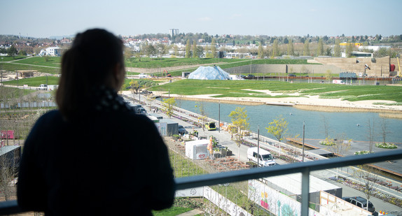 Eine Frau schaut von einem Balkon eines Wohngebäudes der Stadtausstellung auf das Gelände der Bundesgartenschau (Bild: © picture alliance/Sebastian Gollnow/dpa)