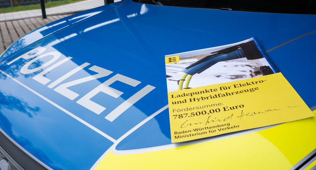 Motorhaube eines Polizeiautos, auf welcher ein Förderbescheid des Verkehrsministeriums für Ladepunkte für Elektro- und Hybridfahrzeuge in Höhe von 787.500 Euro liegt.