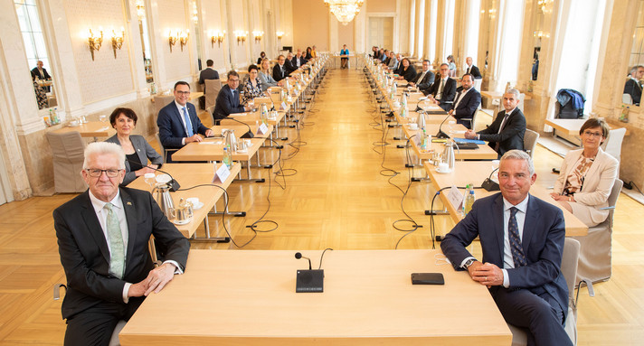 Beschreibung vom Bild: Man blick von vorne in einen Raum im Neuen Schloss in Stuttgart. In dem Raum waren die Sitzungen der Regierung. Auf dem Bild sieht man alle Minister und Ministerinnen vom Land Baden-Württemberg. Das Bild ist von der ersten Sitzung der neuen Regierung im Mai 2022.