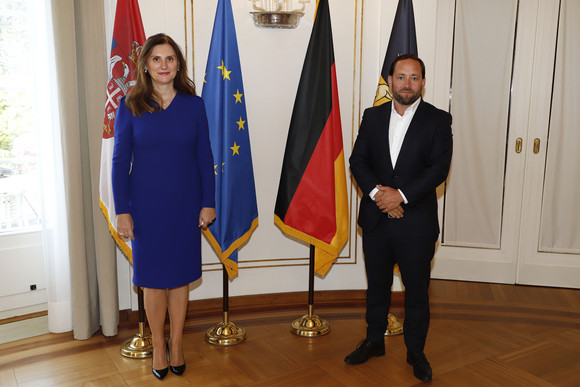 Staatssekretär Florian Hassler (r.) und die serbische Botschafterin Snežana Janković (l.) stehen in der Villa Reitzenstein in Stuttgart vor Fahnen.