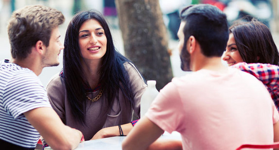 Eine Gruppe junger Menschen sitzt in einem Straßencafe (Bild: © iStock).