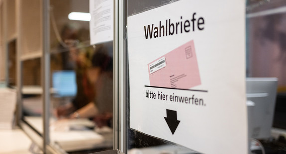 Ein Schild weist in einem Wahlbüro auf eine Wahlurne für die Briefwahl  hin.