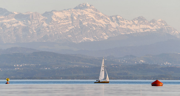 Ein Boot segelt vor Fischbach bei Friedrichshafen auf dem Bodensee, während im Hintergrund das Schweizer Ufer und die Alpen zu sehen sind (Bild: © dpa). 