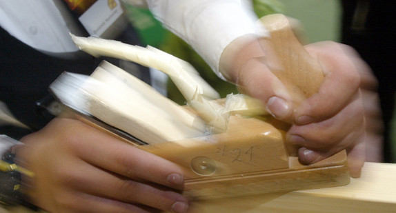 Ein Zimmermann hobelt ein Stück Holz.