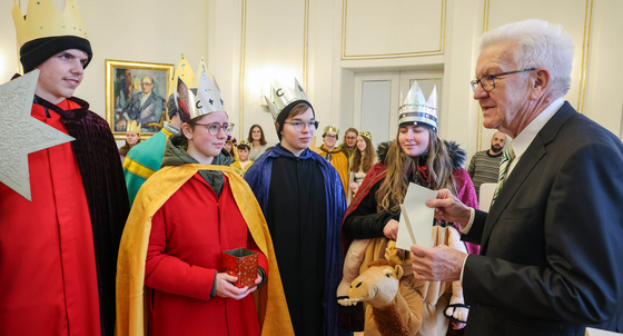 Ministerpräsident Winfried Kretschmann (rechts) überreicht Sternsingerinnen und Sternsingern einen Umschlag.