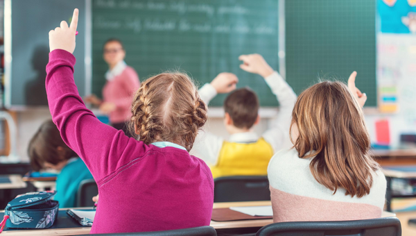 Schülerinnen und Schüler heben im Schulunterricht die Hände.