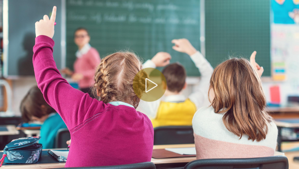 Schülerinnen und Schüler heben im Schulunterricht die Hände.