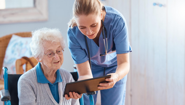 Eine junge Pflegerin zeigt einer älteren Patientin auf dem Tablet medizinische Ergebnisse.