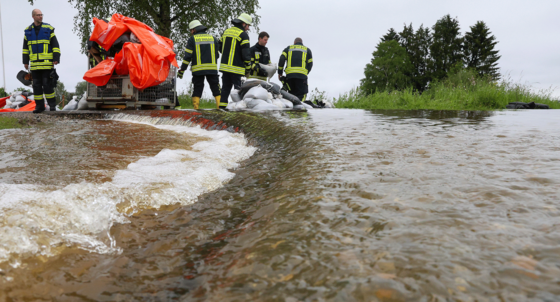 Einsatzkräfte der Feuerwehr errichten am Nonnenbach in Bad Saulgau im Ortsteil Moosheim einen Damm mit Sandsäcken gegen das Hochwasser.