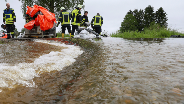 Einsatzkräfte der Feuerwehr errichten am Nonnenbach in Bad Saulgau im Ortsteil Moosheim einen Damm mit Sandsäcken gegen das Hochwasser.