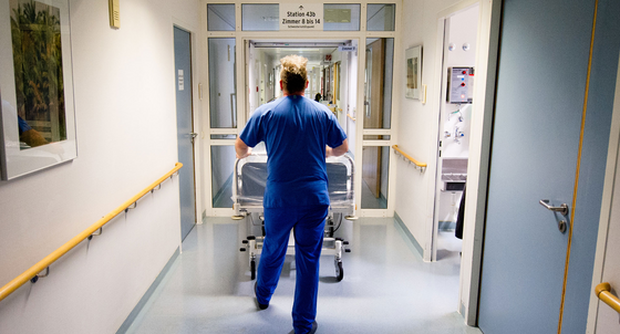 Ein Krankenpfleger schiebt in einer Klinik ein Krankenbett über einen Flur. (Foto: © dpa)